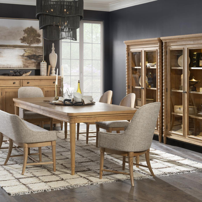 Light wood dining set with gray upholstered dining room benches and chairs, sideboard, and glass display cabinets in a dark blue room.