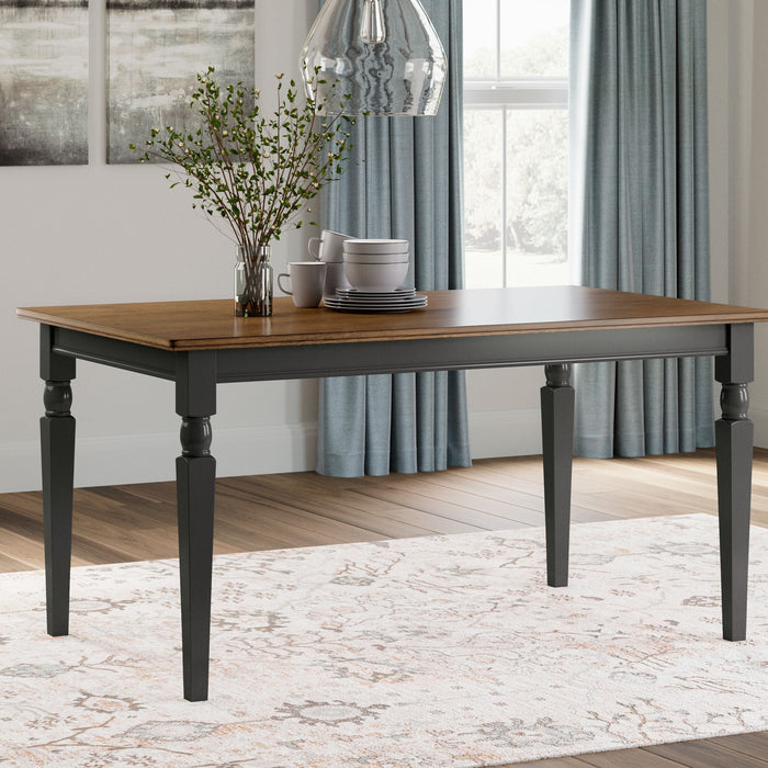 A black/brown rectangular dining room table with flowers in a vase and plates on top.