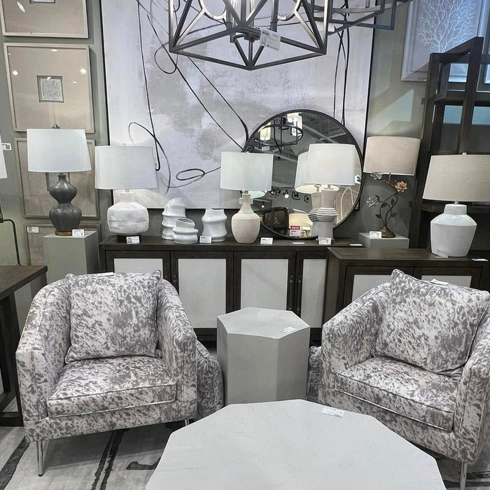 Modern living room with two patterned armchairs, a geometric coffee table, and decorative lamps.